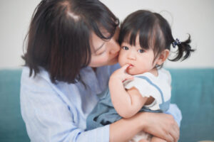 お母さんに抱かれた女の子が指しゃぶりをしている写真
